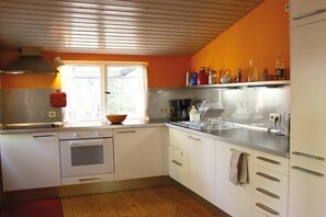 A kitchen with white cabinets, a stove, a sink, and a window with a view of greenery. - Holiday home in Mölln with swimming pool (Mölln)