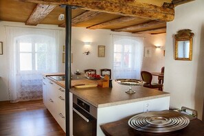 Eine Küche mit Holzbalken, einer zentralen Kochinsel und einem Essbereich mit Stühlen.