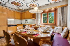 A dining area with a wooden table set for four, a chandelier, and a window with a view of greenery.