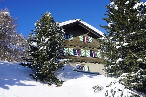A chalet-style building with a sloped roof, surrounded by snow-covered trees.