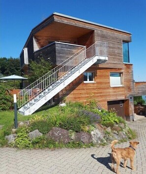 Ein modernes, zweistöckiges Haus mit Holzfassade, einer Metalltreppe und einer kleinen Veranda.