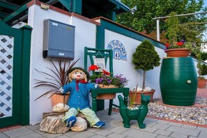 Un jardin avec une statue d’épouvantail, une chaise verte, une plante en pot et un tonneau vert.