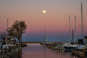 Un port de plaisance au crépuscule, avec des bateaux amarrés, un arbre et un bâtiment en arrière-plan.