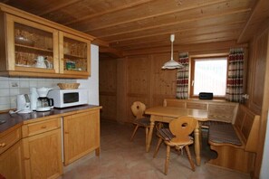 Ein Interieur einer Holzhütte mit Küchenzeile, Holzschränken, einem Esstisch und einem Fenster mit Vorhängen.