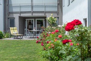 Ein modernes Gebäude mit Balkon, einem Essbereich inklusive Tisch und Stühlen sowie einem gepflegten Garten mit Rosen.