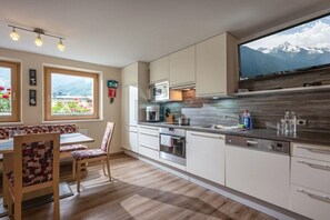 Eine moderne Küche mit einem großen Fenster, Holzboden und einem Essbereich mit Tisch und Stühlen.