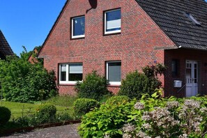 Ein rotes Backsteinhaus mit zwei Fenstern, einer Tür und einem kleinen Garten.