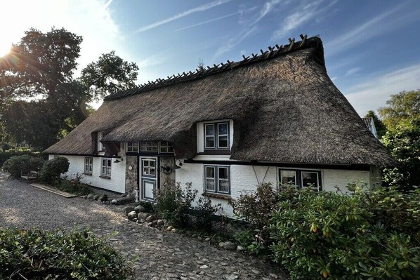 Ein traditionelles Reetdachhaus mit Steinunterbau, einer kleinen Veranda und einem Schotterweg.