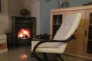 A living room with a fireplace, a white leather armchair, and a wooden cabinet. - Holiday home with 2 bedrooms (Parey\/Elbe)