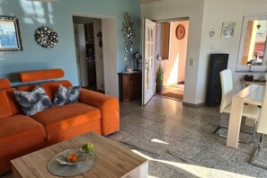 A living room with an orange sofa, a wooden coffee table, and a dining area with a white table and chairs. - Holiday home with 2 bedrooms (Parey\/Elbe)