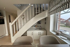 Ein modernes Interieur mit einer weißen Treppe, Korbmöbeln und Blick auf die Straße durch ein Fenster.