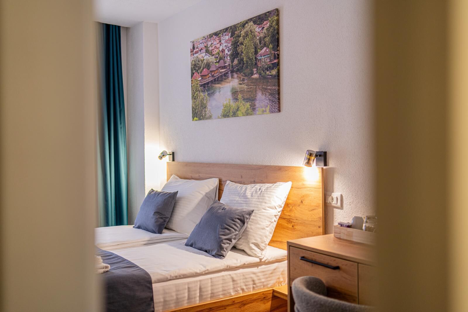 A hotel room with a bed, bedside table, lamp, and a painting on the wall.