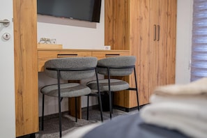 Un dormitorio con cama, armario de madera, escritorio con dos sillas y televisor en la pared.