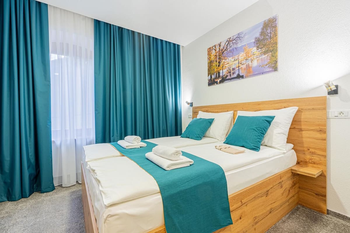 Une chambre d’hôtel avec un lit double, des rideaux de couleur turquoise, une tête de lit en bois et un tableau au mur.