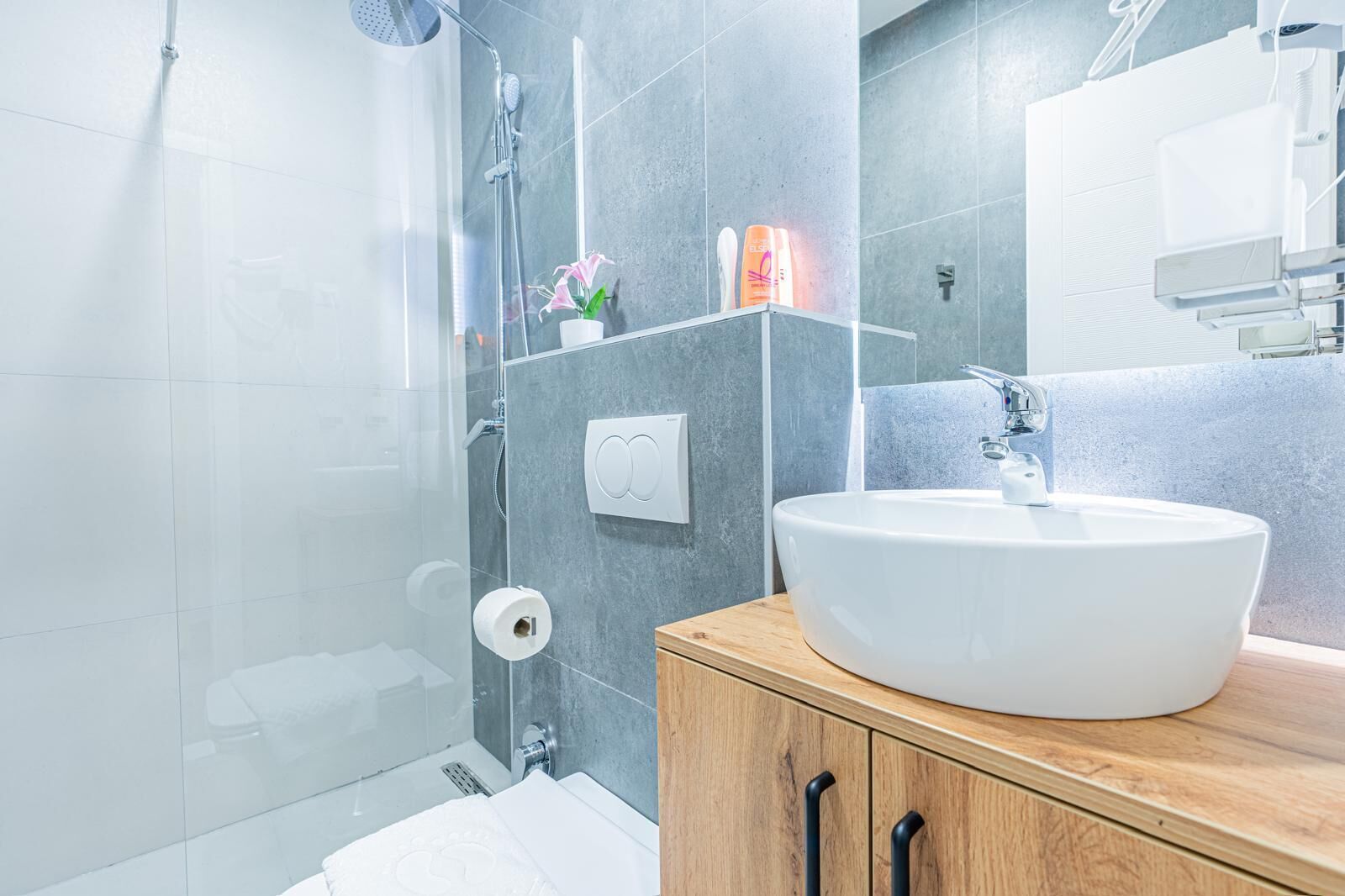 A modern bathroom with a glass shower enclosure, a white sink, and a wooden vanity.