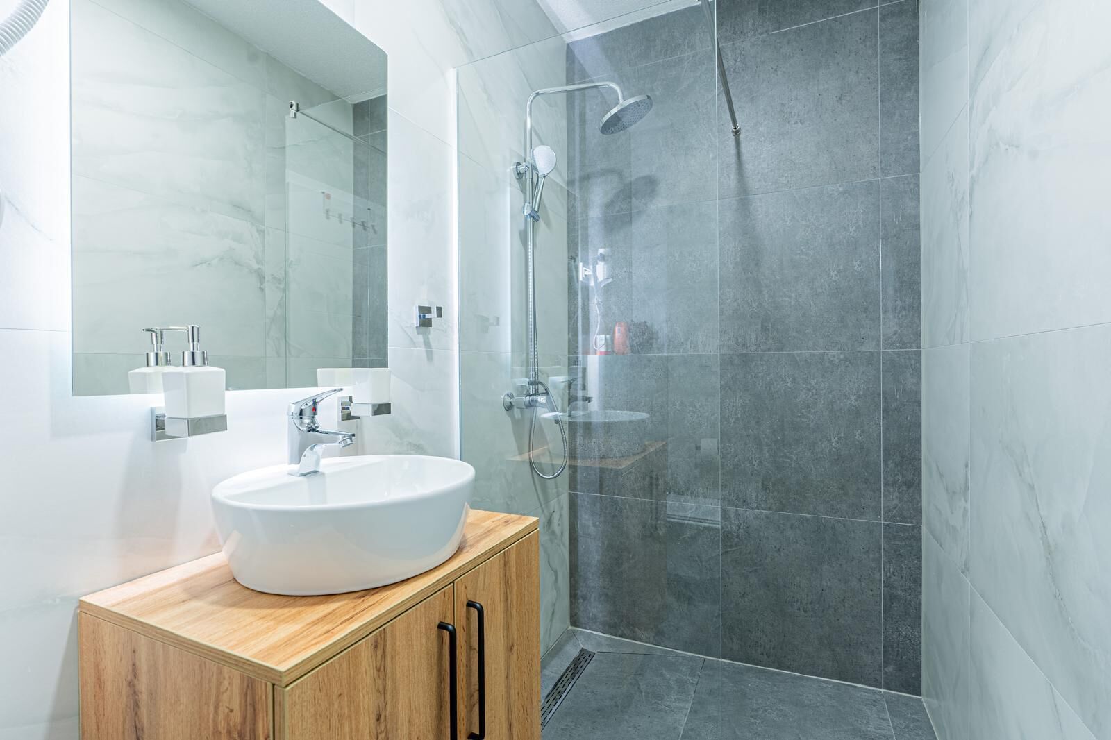 Ein modernes Badezimmer mit einem weißen Waschbecken, einem Holzkabinet und einer Duschkabine aus Glas.