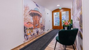 A hallway with a mural of a traditional building, a wooden door, and a green chair with a vase of flowers. - Hotel Una (Sarajevo)