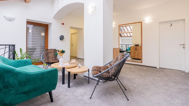 A modern interior with a high ceiling, a skylight, a green sofa, a leopard print chair, and a small table with a vase. - Hotel Una (Sarajevo)