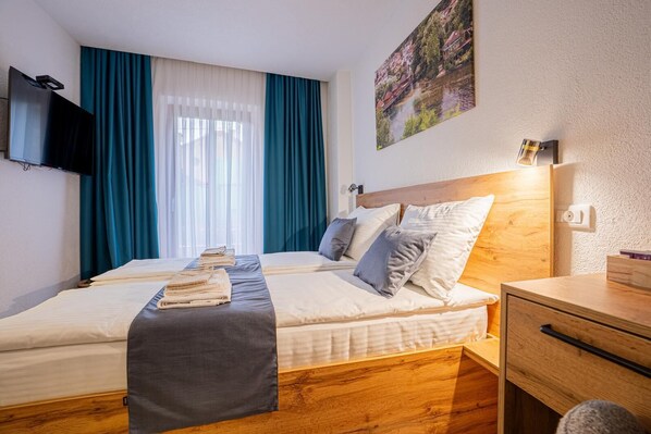 A hotel room with a bed, a TV, a wooden nightstand, and a painting on the wall.
