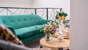 A teal sofa, a round wooden table with a vase of flowers, and a white vase with green foliage. - Hotel Una (Sarajevo)