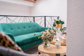 Ein blaugrünes Sofa, ein Couchtisch aus Holz mit einem Blumenstrauß und eine weiße Vase mit Grünpflanzen.
