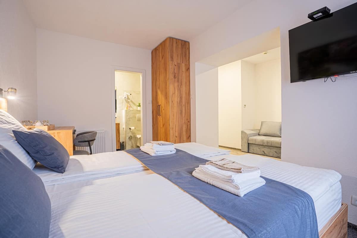 Une chambre d’hôtel avec deux lits, une armoire en bois, un bureau avec une chaise, une télévision et une salle de bain visible à travers une porte ouverte.