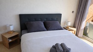 Una cama bien tendida con un cabecero oscuro, dos mesitas de noche con lámparas y una ventana con cortinas.