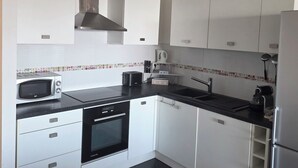 Una cocina moderna con armarios blancos, encimera negra, microondas, tostadora y refrigerador de acero inoxidable.