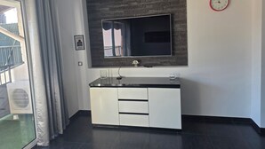 Una habitación moderna con un espejo grande, un televisor de pantalla plana, un armario blanco y un reloj en la pared.