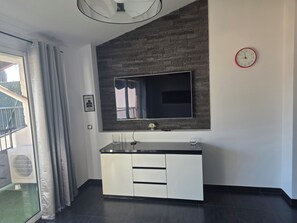 Ein modernes Zimmer mit einem großen Spiegel, einem Flachbildfernseher, einem weißen Schrank und einer Wanduhr.