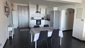 Una cocina moderna con armarios blancos, horno empotrado y refrigerador. Hay un comedor con mesa y sillas.