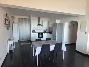 Eine moderne Küche mit weißen Schränken, einem eingebauten Backofen und einem Kühlschrank. Es gibt einen Essbereich mit einem Tisch und Stühlen.