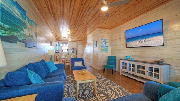 Ein Holzinterieur mit einer Couch, Sesseln, einem Fernseher und Kunstwerken an den Wänden.