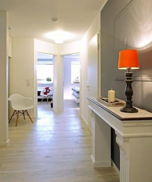 A hallway with a white chair, a table with a red object, and a lit lamp. - Holiday apartment in Juist with swimming pool (Juist)