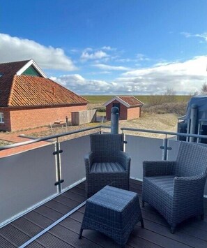 A balcony with wicker chairs and a small table, overlooking a building with a red roof and a chimney. - Holiday apartment in Juist with swimming pool (Juist)