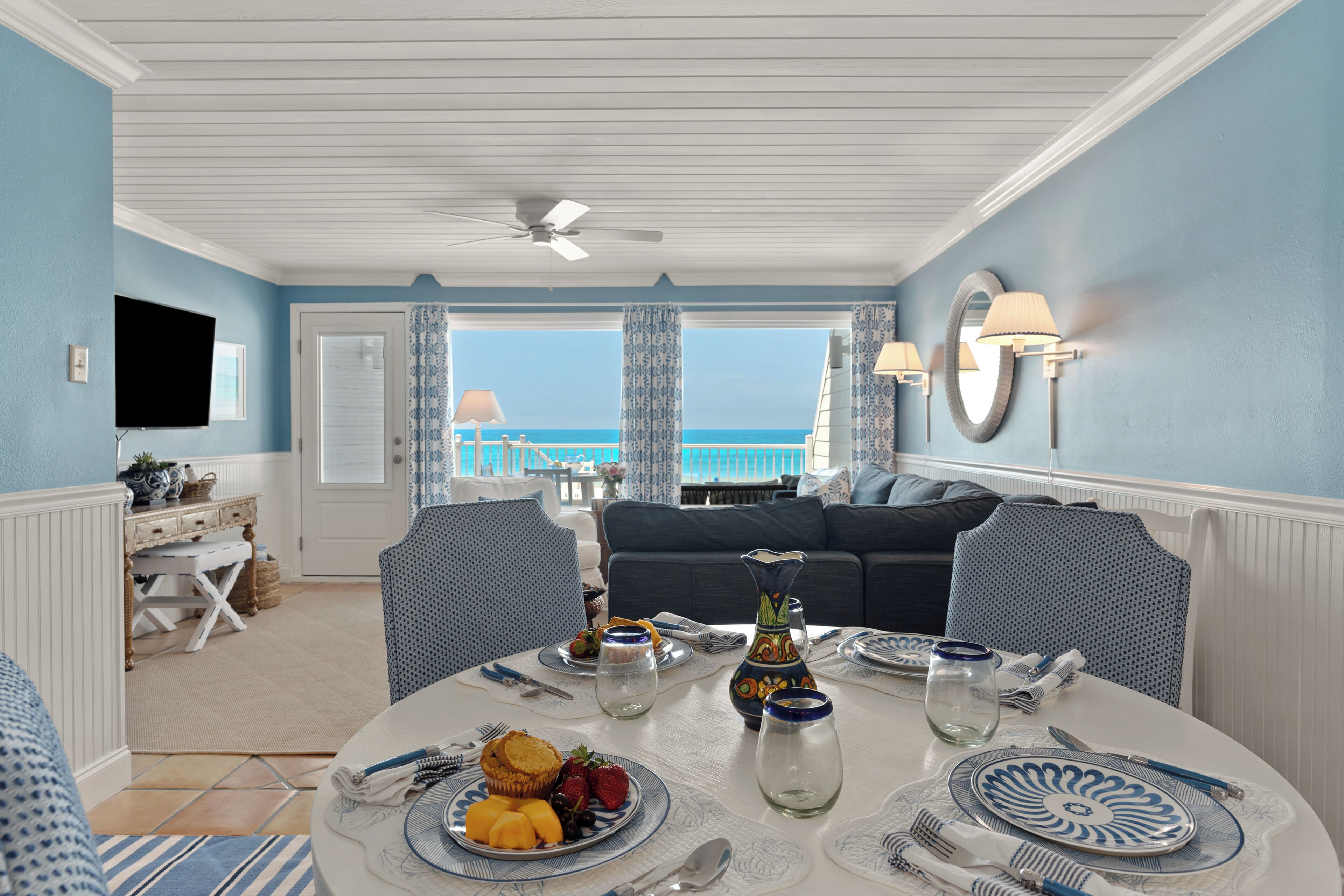 A dining area with a table set for four, a view of the ocean, and a ceiling fan.