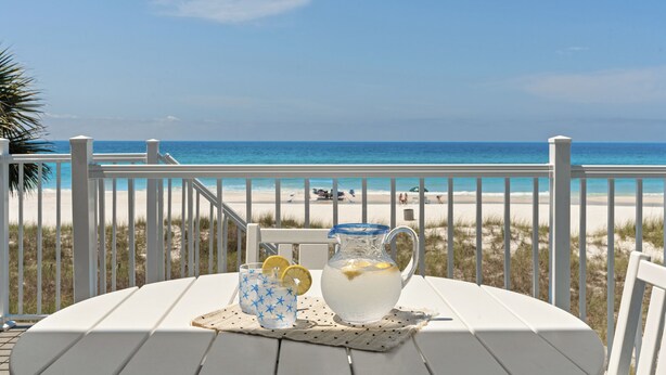 Une table avec une carafe et des verres, placée sur une terrasse donnant sur une plage.