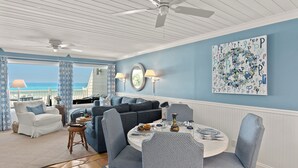 Un salon avec vue sur l’océan, un coin repas avec une table ronde et un ventilateur de plafond.