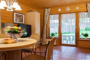 Ein Holzinnenraum mit einem Esstisch, Stühlen, einem Fernseher und Blick ins Freie.
