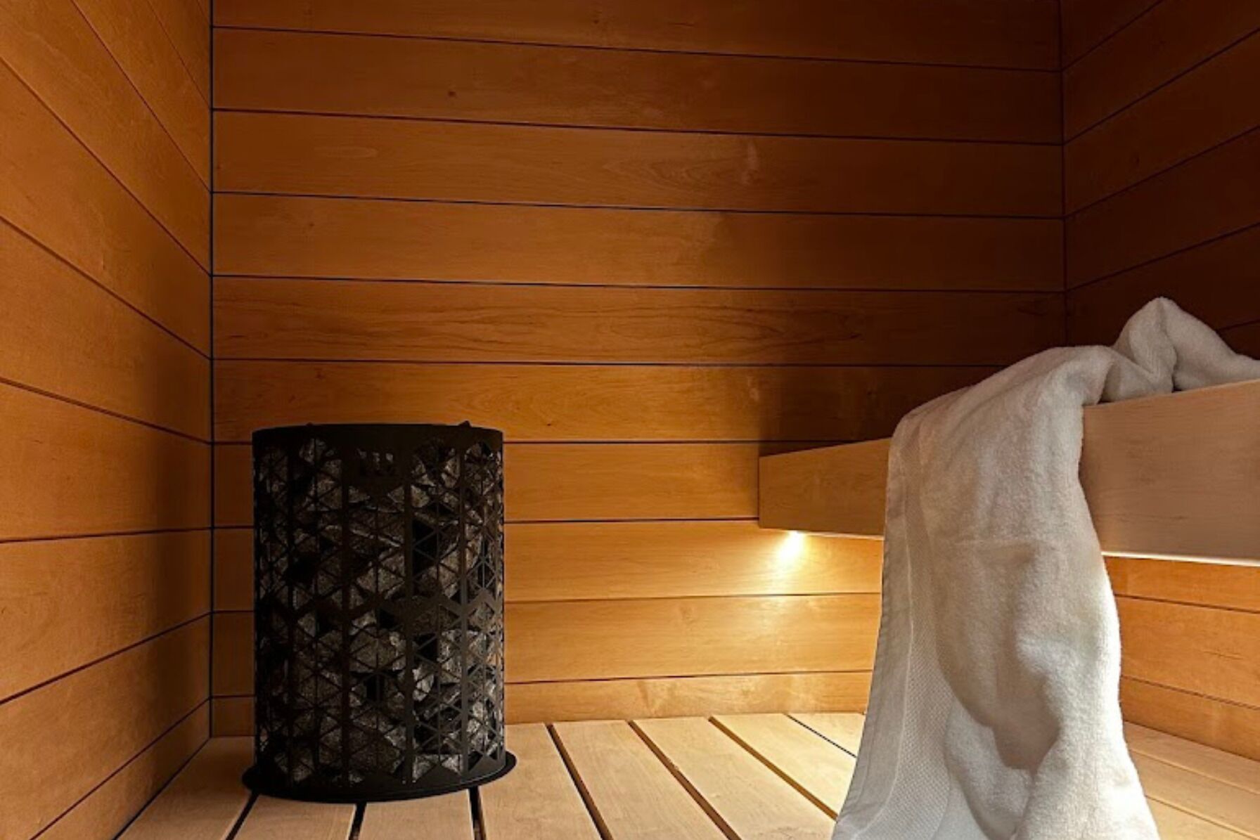Un sauna aux murs en bois, un récipient décoratif noir et une serviette blanche.