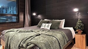 Een slaapkamer met een groot raam, donkere houten wanden, een bed met groene beddengoed en een kleine kerstboom.