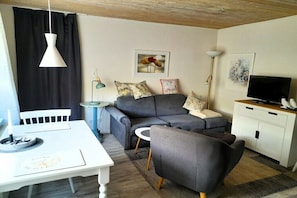 Ein Wohnzimmer mit Sofa, Fernseher, Esstisch und einem kleinen Beistelltisch.