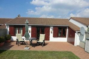 A house with a tiled roof, a patio with a table and chairs, and a satellite dish. - Holiday home in De Haan with swimming pool (De Haan)