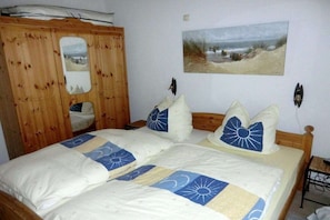 A bedroom with a wooden wardrobe, a bed with patterned bedding, a wall-mounted picture, and a bedside table. - Holiday home in De Haan with swimming pool (De Haan)