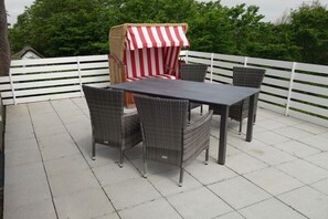 A patio with a table and chairs, a striped awning, and a white fence. - "Seagull under thatch" (Nebel)