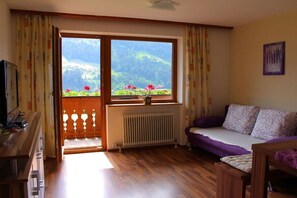 Ein Zimmer mit Holzboden, einer Couch, einem Tisch, einem Heizkörper und einem Fenster mit Blick auf Grünflächen.