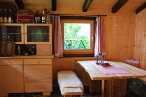 Ein Holzblockbau-Innenraum mit Holztisch, Bank und einem Fenster mit Vorhängen.