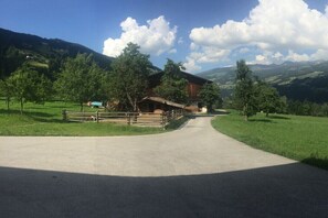 Ein Feldweg führt zu einem Holthaus mit umzäunter Wiese und Bäumen.