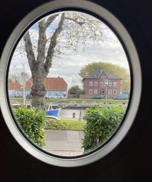 Blick durch ein Fenster auf einen Baum, ein rotes Gebäude und ein blaues Boot.