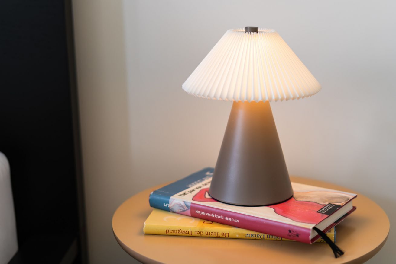 Abajur com cúpula franzida sobre uma pequena mesa com livros.